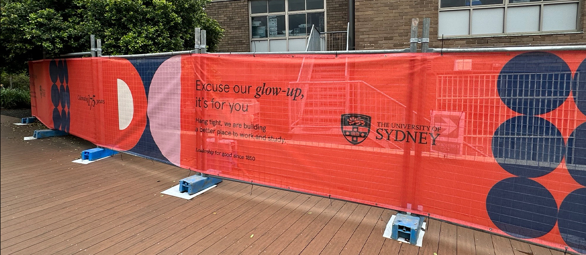 Mesh fence hoarding with the University of Sydney logo and text that says: 'Excuse our glow-up, it's for you. Hang tight, we are building a better place to work and study.