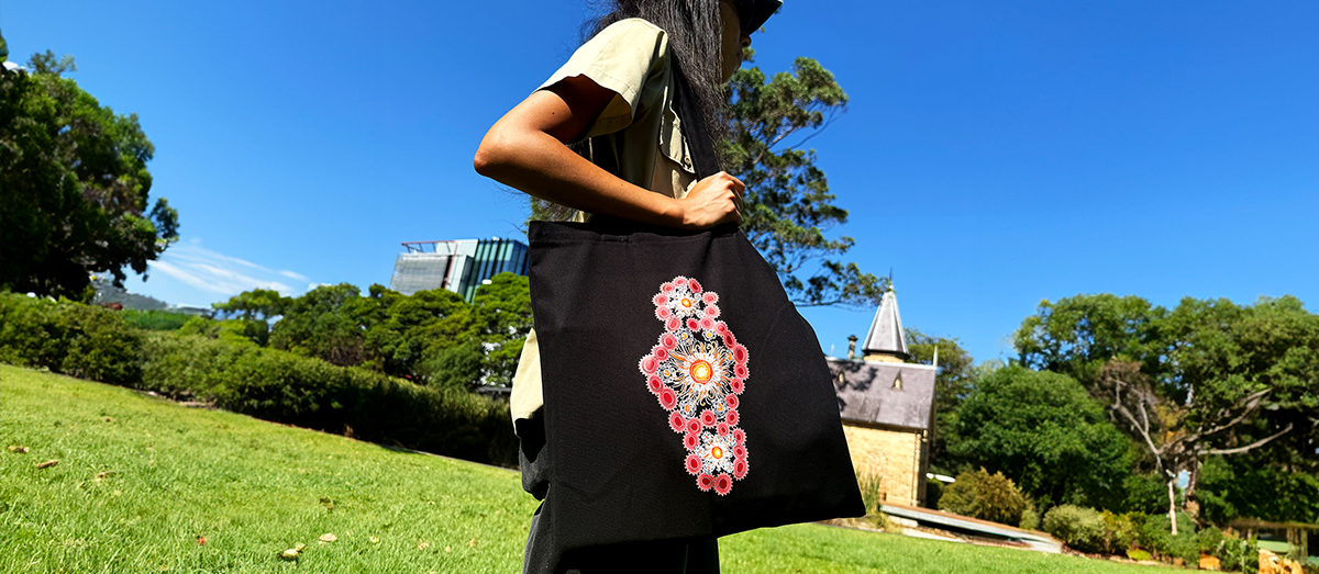 Student holding a black tote bag with a pink, white and orange design on the front