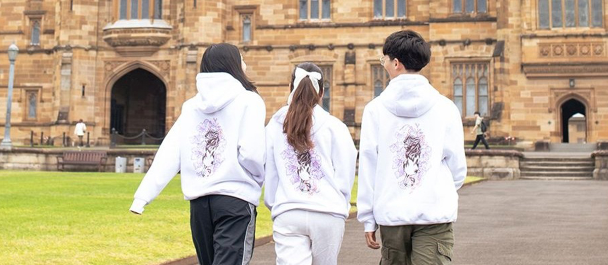 three students stand in front of The Quad wearing the 2024 winning hoodie design