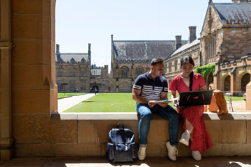 Two students sitting in the quad looking at a laptop