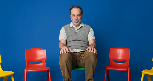 A man sitting on a chair against a blue backdrop