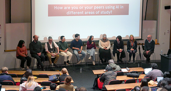 Several people sitting on chairs in a row behind a screen in front of a lecture theatre of audience members