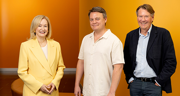 Judy Harris, Luke Carman and Professor Stephen Simpson in front of a yellow backdrop.