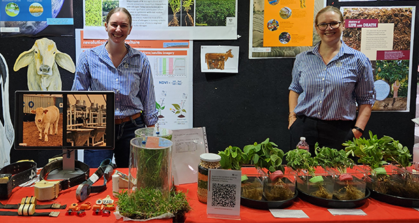 Two people standing at a stall with various plants and information around them.