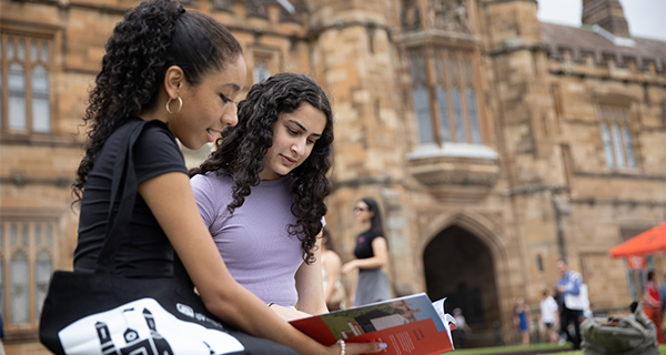 two students in front of the Quad reading an Info Day brochure