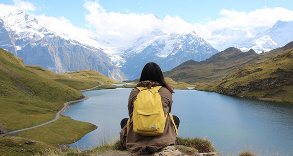 A person with a yellow backpack sitting in front of Lake Bachalpsee in Switzerland.