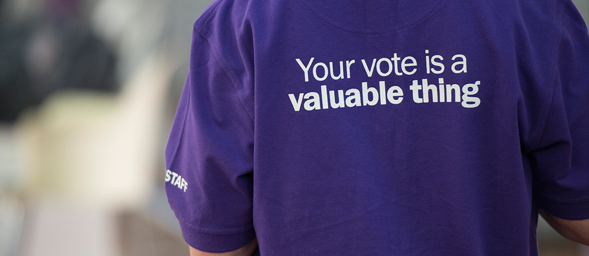 A person working at the election wearing a purple shirt that says 'Your vote is a valuable thing'.