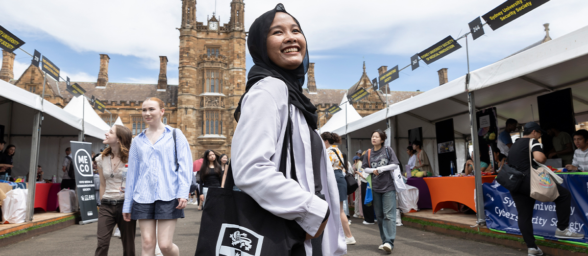 Student standing in between stalls with the Quadrangle clock tower behind them
