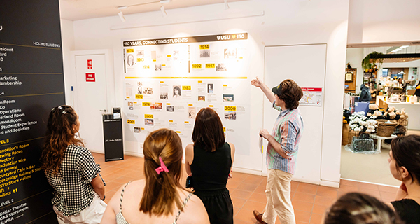 A tour guide pointing towards a decal on the wall with people looking towards where they're pointing