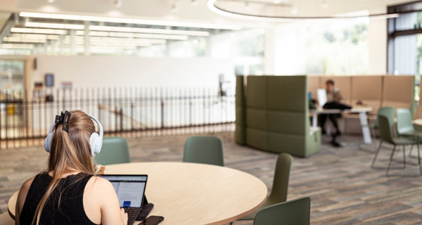 A student on their laptop with headphones on at a desk in a study space