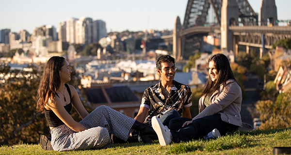 A group of students sitting in a park with the harbour bridge in view