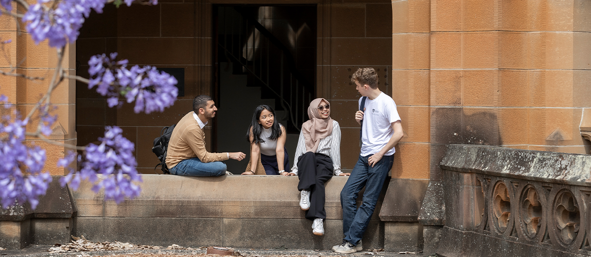 Students chatting in the Quadrangle with a flowering jacaranda branch in the foreground  